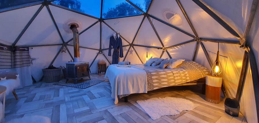 Intérieur d'un dôme glamping avec lit double, poêle à bois et éclairage tamisé à l'Astronarium Aniane